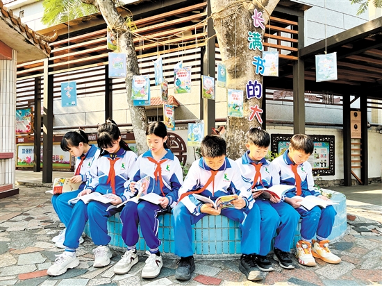 龍口鎮(zhèn)協(xié)華小學(xué)學(xué)生圍坐在“長(zhǎng)滿書的大樹”下捧書共讀，成為該校一道亮麗的風(fēng)景線。